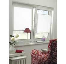 Store plissé blanc sur une fenêtre à deux vantaux dans une pièce lumineuse avec fauteuil rouge, petite table et fleurs.