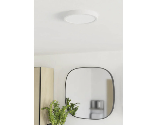 Plafonnier LED rond et plat installé dans une pièce lumineuse avec miroir et plante.
