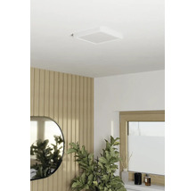 Plafonnier LED carré sur un plafond blanc dans une pièce moderne avec des panneaux muraux en bois, un miroir et une plante verte.