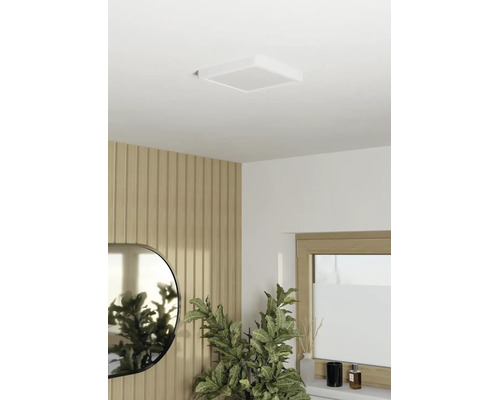Plafonnier LED carré sur un plafond blanc dans une pièce moderne avec des panneaux muraux en bois, un miroir et une plante verte.