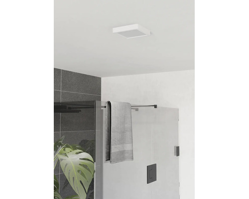 Modernes Badezimmer mit quadratischer Deckenleuchte, Glasduschwand mit schwarzen Beschlägen, grauem Handtuch und dunklen Wandfliesen.