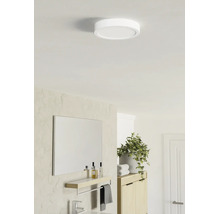 Plafonnier LED rond et plat dans une salle de bains lumineuse au design moderne avec miroir, étagère et plante.