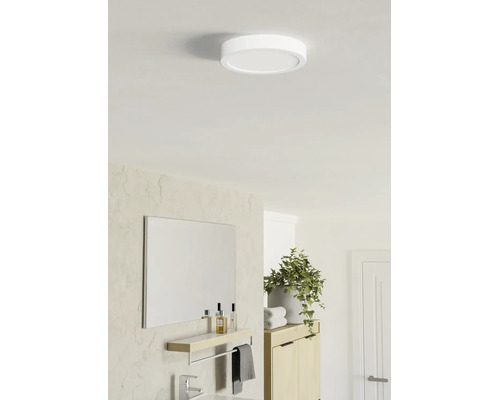 Plafonnier LED rond et plat dans une salle de bains lumineuse au design moderne avec miroir, étagère et plante.