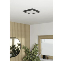 Plafonnier LED carré dans une pièce lumineuse au design moderne avec des panneaux muraux imitation bois, un miroir ovale et une plante d'intérieur.