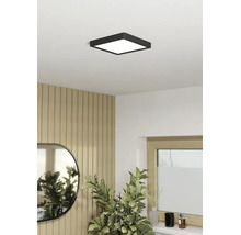 Plafonnier LED carré noir dans une pièce lumineuse avec mur en panneaux de bois, miroir et plante verte.