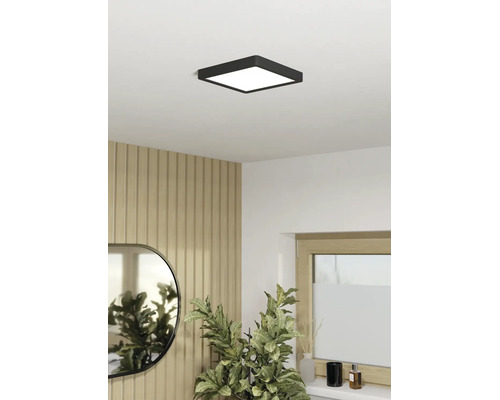 Plafonnier LED carré noir dans une pièce lumineuse avec mur en panneaux de bois, miroir et plante verte.