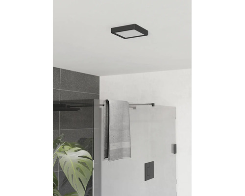 Scène de salle de bains moderne avec plafonnier LED carré noir, douche en verre, carrelage gris et plante verte.