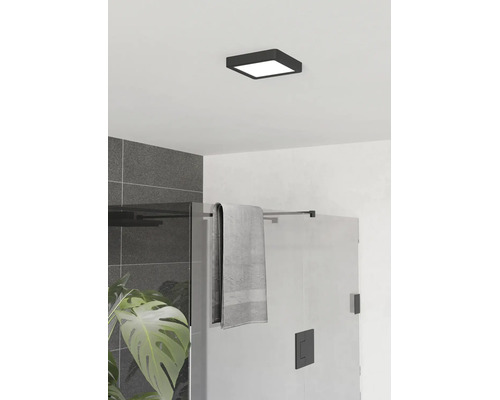 Plafonnier carré et plat noir dans une salle de bain moderne avec douche en verre et carrelage gris.