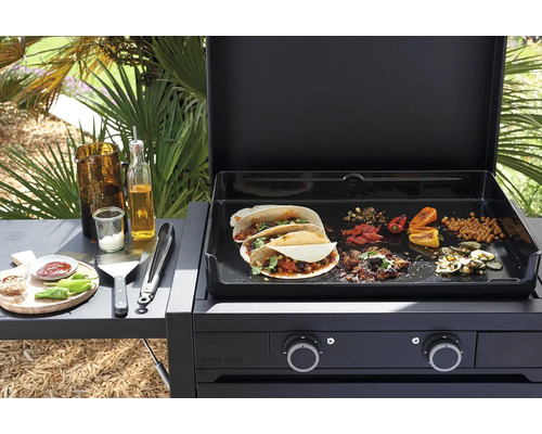 Forge Adour Gas-Plancha mit geöffnetem Deckel, Tacos und Gemüse auf der Grillfläche sowie Grillzubehör auf der seitlichen Ablage.