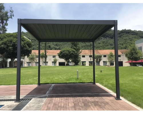 Freistehende Pergola aus Aluminium mit Lamellendach auf einer Holzterrasse im Garten vor einer Grünfläche.