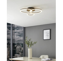 Plafonnier LED moderne à quatre anneaux lumineux dans une pièce lumineuse avec mur gris, vue sur la ville et table blanche.