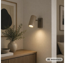 Applique murale avec abat-jour cylindrique en bois strié, diffusant une lumière chaude vers le bas sur un mur.