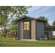 Graues Gartenhaus aus Holz mit Satteldach und Tür mit Fenstereinsatz in einem hellen, organisierten Garten mit Rasen, Holzrad und Steinmauer.