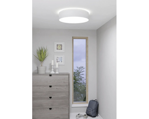 Plafonnier rond blanc dans une pièce moderne avec une commode, une plante et une fenêtre étroite.