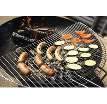 Une grille de barbecue ronde en métal sur du charbon de bois et des bûches en feu, avec des saucisses, des tranches de courgettes et des poivrons.