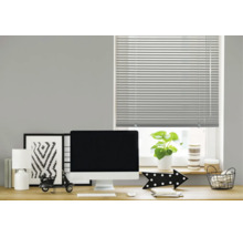Un store vénitien horizontal sur une fenêtre au-dessus d'un bureau moderne avec écran, lampe et décoration dans un bureau.