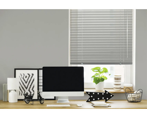 Un store vénitien horizontal sur une fenêtre au-dessus d'un bureau moderne avec écran, lampe et décoration dans un bureau.