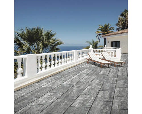 Terrasse moderne avec dalles en aspect pierre grise, balustrade blanche, chaises longues et vue sur mer dans un cadre méditerranéen lumineux.