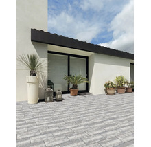 Terrasse lumineuse avec pavés gris rectangulaires modernes, décorée de bacs à plantes et de lanternes contre une façade blanche.