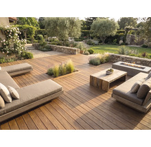 Grande terrasse en bois avec salon de jardin moderne, table en bois, foyer extérieur et murs en pierre naturelle dans un jardin soigné.