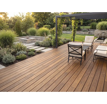Terrasse en bois moderne, lames foncées, salon de jardin en métal, coussins clairs, pergola et foyer maçonné dans un jardin soigné.