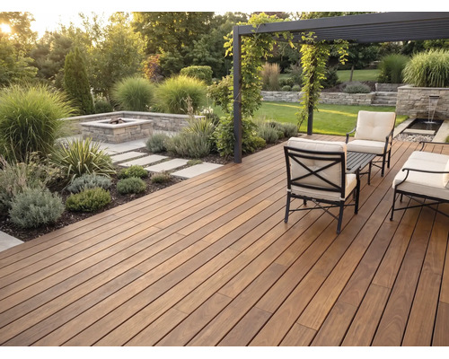 Terrasse en bois moderne, lames foncées, salon de jardin en métal, coussins clairs, pergola et foyer maçonné dans un jardin soigné.