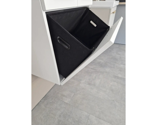 Meuble sous-vasque avec tiroir basculant ouvert et panier à linge en textile noir.