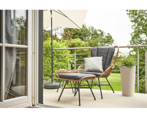 Moderner Balkon mit Lounge-Sessel aus Geflecht, Hocker, grauen Kissen, Sonnenschirm, Beistelltisch und Pflanzgefäß mit Blick in den Garten.