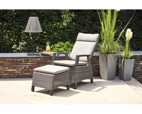 Fauteuil de jardin en polyrotin avec pouf assorti et coussins clairs sur une terrasse moderne avec de hauts bacs à fleurs.