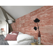 Helles Schlafzimmer mit strukturierter Wand in roter Holzoptik, weissem Bettzeug, rustikalem Holzbalken und einer modernen Stehlampe.