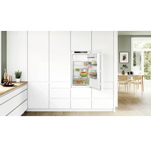 Réfrigérateur encastrable dans une cuisine blanche moderne avec porte ouverte et aliments, dans une ambiance lumineuse et chaleureuse.