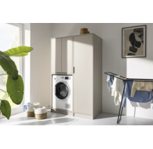 Meuble moderne pour lave-linge et armoire haute beige dans une buanderie lumineuse et ordonnée avec séchoir à linge et plante.