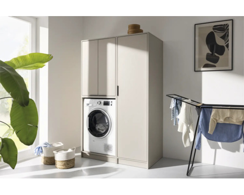 Meuble moderne pour lave-linge et armoire haute beige dans une buanderie lumineuse et ordonnée avec séchoir à linge et plante.