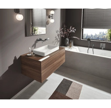 Modernes Badezimmer mit Waschtisch in Holzoptik, weissem Aufsatzwaschbecken, integrierter Badewanne, Wandarmaturen und stimmungsvoller Beleuchtung.