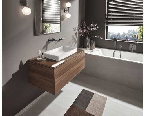 Modernes Badezimmer mit Waschtisch in Holzoptik, weissem Aufsatzwaschbecken, integrierter Badewanne, Wandarmaturen und stimmungsvoller Beleuchtung.