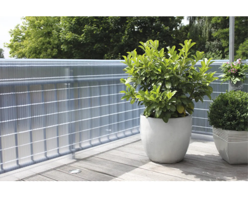 Balcon avec pare-vue en plastique sur une rambarde en métal, au premier plan deux pots de fleurs avec des plantes sur un sol en bois.