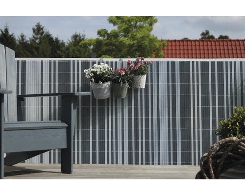 Brise vue de balcon en lamelles plastiques sur une rambarde avec des pots de fleurs suspendus et des meubles de jardin.