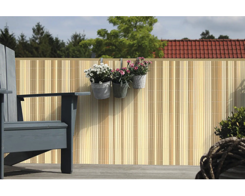 Brise vue de balcon en tiges de bambou sur une terrasse avec des pots de fleurs suspendus et un fauteuil.