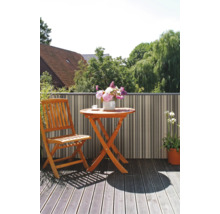 Balcon avec table pliante en bois, chaise pliante en bois et écran de confidentialité rayé sur un sol en bois avec vue sur la verdure.