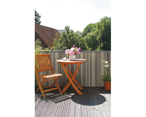 Balcon avec table pliante en bois, chaise pliante en bois et écran de confidentialité rayé sur un sol en bois avec vue sur la verdure.