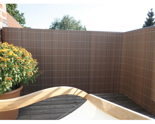 Brise-vue en plastique sur une terrasse en bois avec une plante en pot et un meuble de jardin au premier plan.