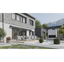 Moderne Terrasse mit Essgruppe vor einem Haus mit Klinkerfassade und Markise sowie einem Außenkamin im gepflegten Garten vor Bergkulisse.