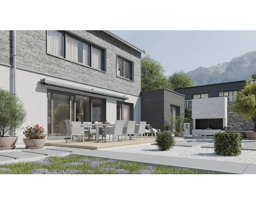 Moderne Terrasse mit Essgruppe vor einem Haus mit Klinkerfassade und Markise sowie einem Außenkamin im gepflegten Garten vor Bergkulisse.