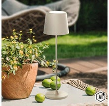 Lampe de table LED sans fil moderne sur une table de jardin à côté d'un pot de fleurs avec des fleurs jaunes et des citrons verts à l'extérieur. (Image AI modified or generated)