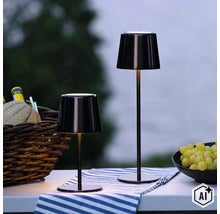 Zwei moderne, schlanke LED Tischleuchten mit Akkubetrieb für den Außenbereich auf einem gedeckten Tisch im Garten. (Image AI modified or generated)