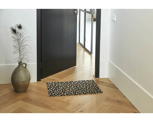 Fussmatte mit Leopardenmuster auf einem Parkettboden in einem hellen Flur mit einer Vase und einer offenen Tür.