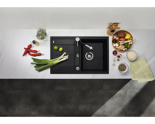 Évier encastrable moderne noir en composite dans une cuisine claire avec robinetterie, entouré de légumes frais et ustensiles de cuisine.