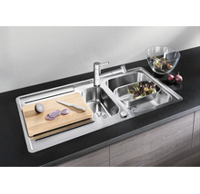 Évier encastrable en acier inoxydable avec deux bacs, robinet, planche à découper et accessoires dans une cuisine moderne.