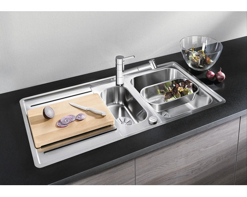 Évier encastrable en acier inoxydable avec deux bacs, robinet, planche à découper et accessoires dans une cuisine moderne.