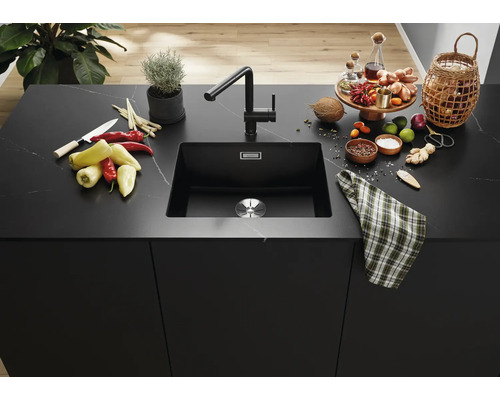 Moderne schwarze Küchenspüle mit passender Armatur in einer eleganten Kücheninsel aus Stein mit Kochzutaten und Dekoration.